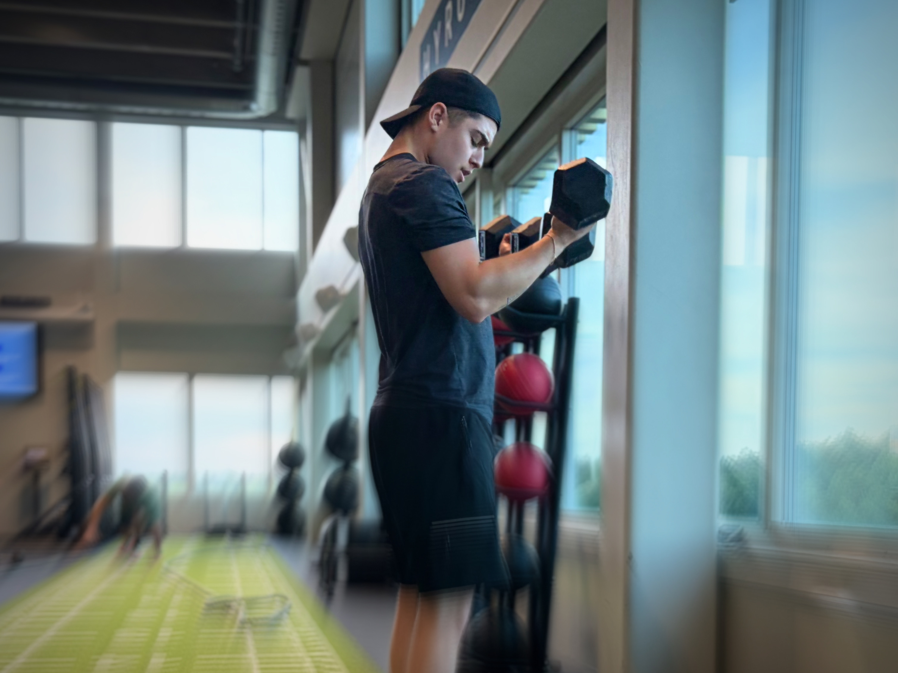 En person gör bicepscurl med hantlar framför ett fönster på gymmet.